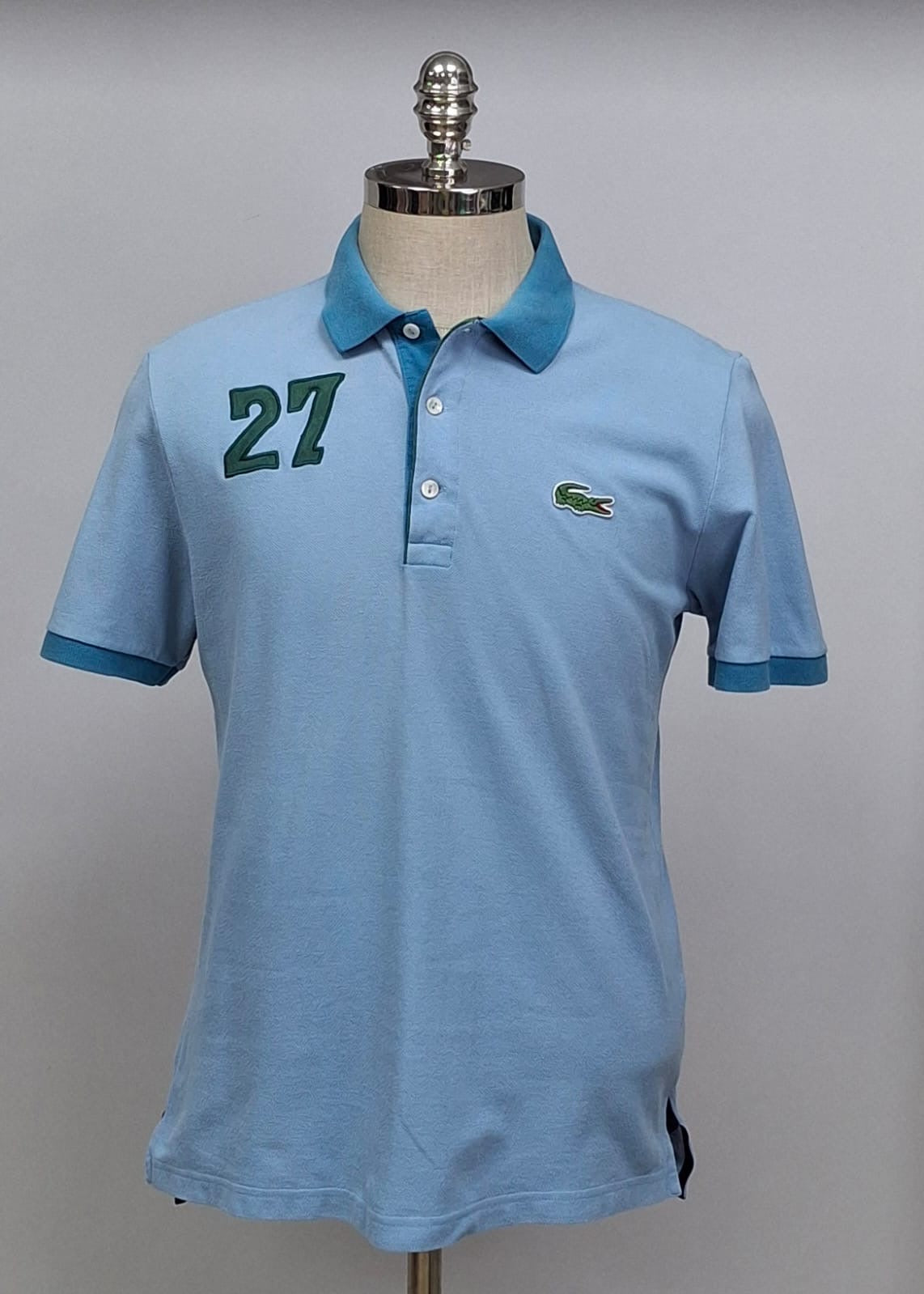 Camiseta Polo Lacoste 🐊 color celeste y diseño en cuello y manga color azul Talla L Entalle Regular
